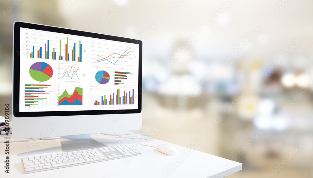 Poster Modern computer with keyboard and mouse on white table showing charts and graph on screen against modern white room  background