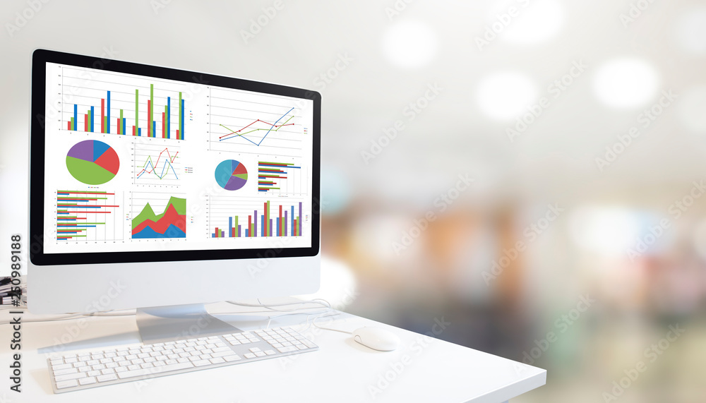 Poster Modern computer with keyboard and mouse on white table showing charts and graph on screen against modern white room  background