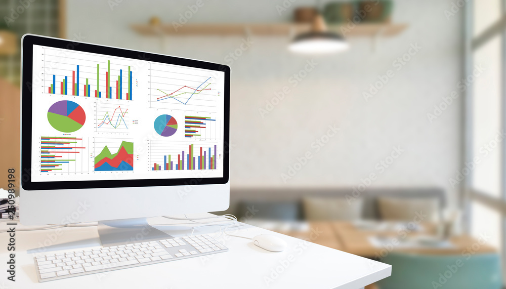 Poster Modern computer with keyboard and mouse on white table showing charts and graph on screen against modern white room  background