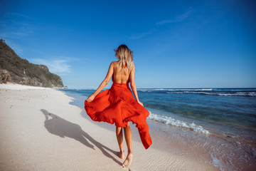 Girl walking on the beach in red dress back view