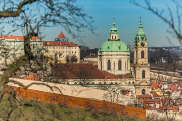 Fototapeta premium Prague, Czech Republic / Europe - February 15 2019: St Nicholas church with dome and a clock tower standing on Lesser Town Square, historical buildings, sunny day, blue sky, view from Petrin hill