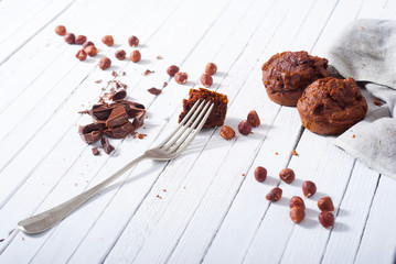 broken chocolate muffin and hazelnuts, fork on white wood table