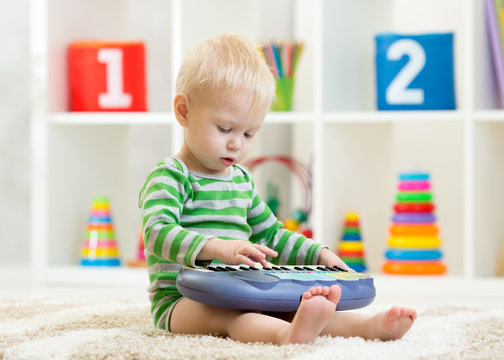 Kid boy plays toy piano sitting on floor in nursery