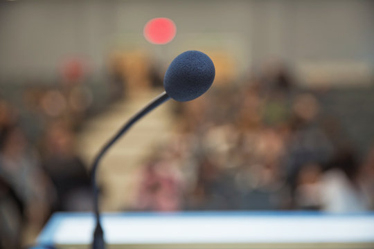 Speaker prepare before speaking to the audience behind the podium focused microphone on the podium and blurred empty seat and some of audience . Speech or conference concept.