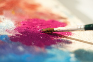 The art brush mixes different oil paints, in this case pink and purple, on a wooden palette