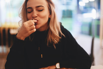 Funny blonde woman in black hoodie eating cheese balls at restaurant.