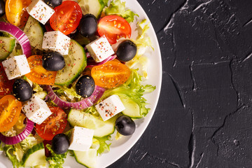 Greek salad with fresh vegetables, feta cheese and black olives on a dark stone slate background. Top view. Free space for your text.