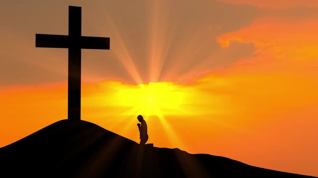 Silhouette of christian man praying to the cross on the hill at sunset time. Shot in 4k resolution