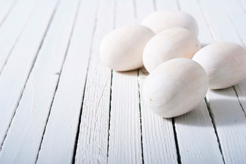 white painted wooden eggs on bright wood table background