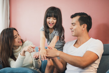 Happy Cheerful smiling Young Family mother father and daughter sitting on the blue sofa and all playing together, rose pink color background wall, stay at home