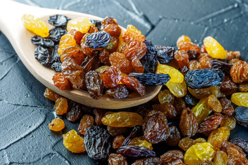 Assortment of Raisins, yellow, blue, black, golden raisin in wooden spoon scattered on dark table...