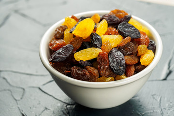 White ceramic bowl with Assortment of Raisins, yellow, blue, black, golden raisin on kitchen table background. Healthy snack. Vega Food. Mix, mixed. Healthy breakfast.