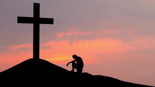 Silhouette of man making confession to the cross on the hill at sunset time. Shot in 4k resolution