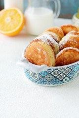 Yeast pancakes in powdered sugar with milk and honey on a light background. Yeast fritters for Sunday breakfast