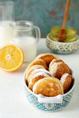 Yeast pancakes in powdered sugar with milk and honey on a light background. Yeast fritters for Sunday breakfast