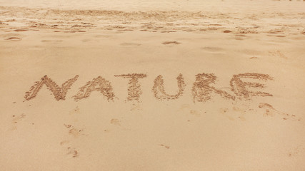 Word NATURE hand written in wet sand of beach.