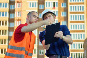 Two engineer builders with blueprint plan at construction site