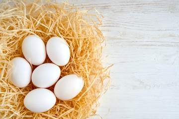 White chicken eggs on straw on a wooden base