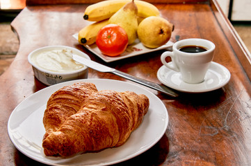 Coffee and croissant breakfast on a vintage wooden table. Espresso, croissants, cream cheese and fruits. 