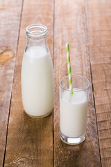 Bottle and glass of milk with straw on wooden table