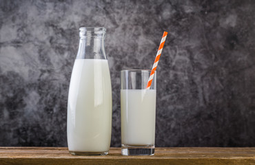 Bottle and glass of milk with straw on wooden table