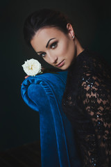 Gorgeous woman in lace dress is holding rose and sits in armchair into expensive room