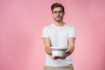 Sad poor young man holding hat and asking for money over pink background.