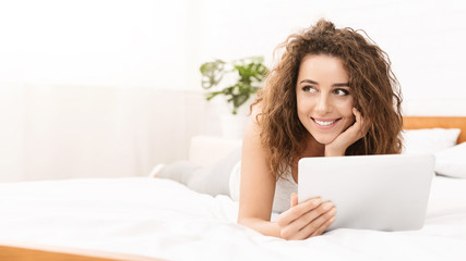 Cheerful young woman lying in bed with tablet