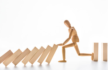 Wooden mannequin stopping domino effect on white