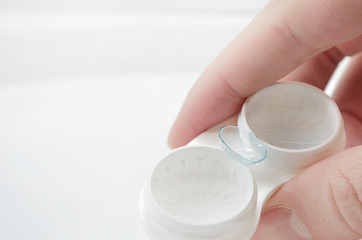 the girl is holding a container for soft contact lenses and a lens on her finger