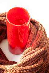  A red glass vase and a knitted brown scarf. Decorative background