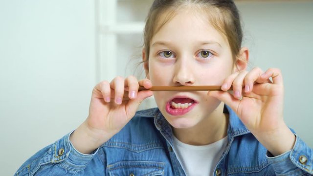 funny little girl making faces with pencil as a moustache and looking at camera