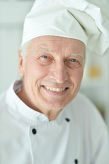 Portrait of happy elderly male chef posing at home