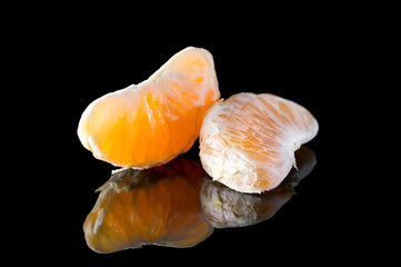 Tangerines or mandarins slices on black reflective background.