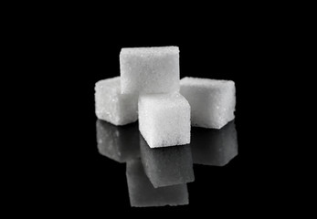 Heap of sugar cubes on black reflective background.