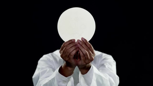 Faceless pastor showing a sacramental bread or communion bread on dark background. Shot in 4k resolution