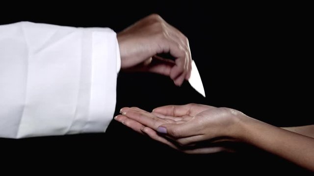 Priest giving first communion bread on woman hands over dark background. Shot in 4k resolution
