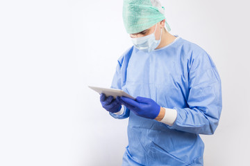 Surgeon doctor in sterile gloves preparing for operation using tablet computer. He is wearing surgical cap and blue gown