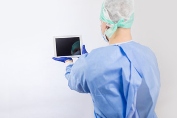 Surgeon doctor in sterile gloves preparing for operation using tablet computer. He is wearing surgical cap and blue gown