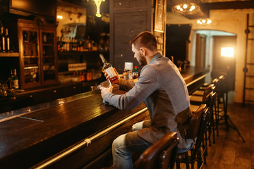 Man with bottle of alcohol at wooden bar counte