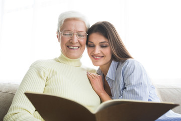 Senior mother and daughter looking photo album at home