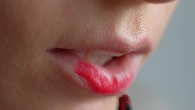 Macro shoot - The girl does makeup on her lips. Applying red lipstick to lips. Beauty saloon. Clean skin. Close-up. 4k.