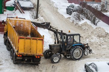 tractor loads the snow in the truck for snow removal from the city