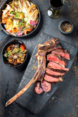 Traditional barbecue dry aged wagyu tomahawk steak sliced with ratatouille and fried mushroom chicory as top view on a rustic carbonized wooden board