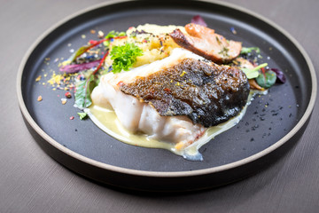 Gebratenes dänisches Skrei Fisch Filet mit Kartoffel Püree, Pilzen und Lemon Curd als closeup auf einem Modern Design Teller