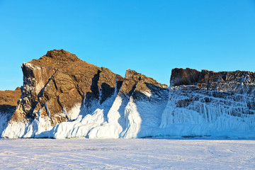 Lake Baikal February sunny day. Rocks of Olkhon Island with white crusts of ice. Winter landscape