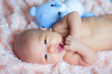 Happy Cute little Asian 2 months old newborn baby boy child is smiling with blue teddy bear toy and looking at camera, Newborn child relaxing in bed. Soft and Selective focus