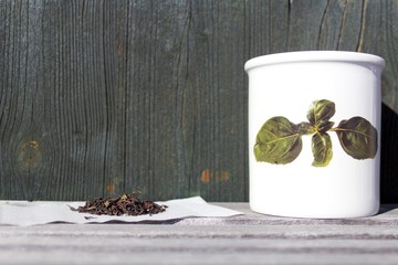 Teedose mit aufgemalzen Teeblättern und geschnittener Tee auf Teefilter vor dunkelgrüner Holzwand