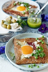 Breton traditional pancake made from buckwheat flour with ham, cheese, egg, feta, green peas and green butter. Breakfast of buckwheat thin pancakes with fried eggs, ham and cheese.