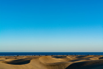 Landscape with yellow sandy dunes of Maspalomas and blue Atlantic ocean, Gran Canaria, Spain